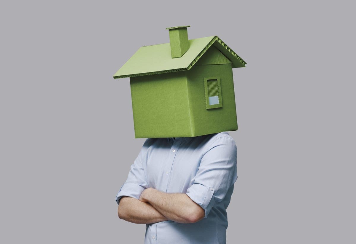 A resident with a cardboard house held over their head — the flat, not the person.
